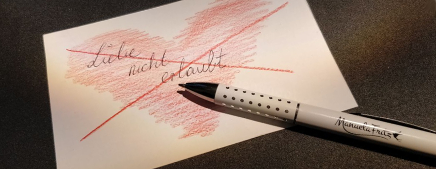 Weißes Blatt mit durchgestrichenem rotem Herz und Schriftzug Liebe nicht erlaubt. Kugelschreiber weiß mit Logo der Autorin Manuela Fritz